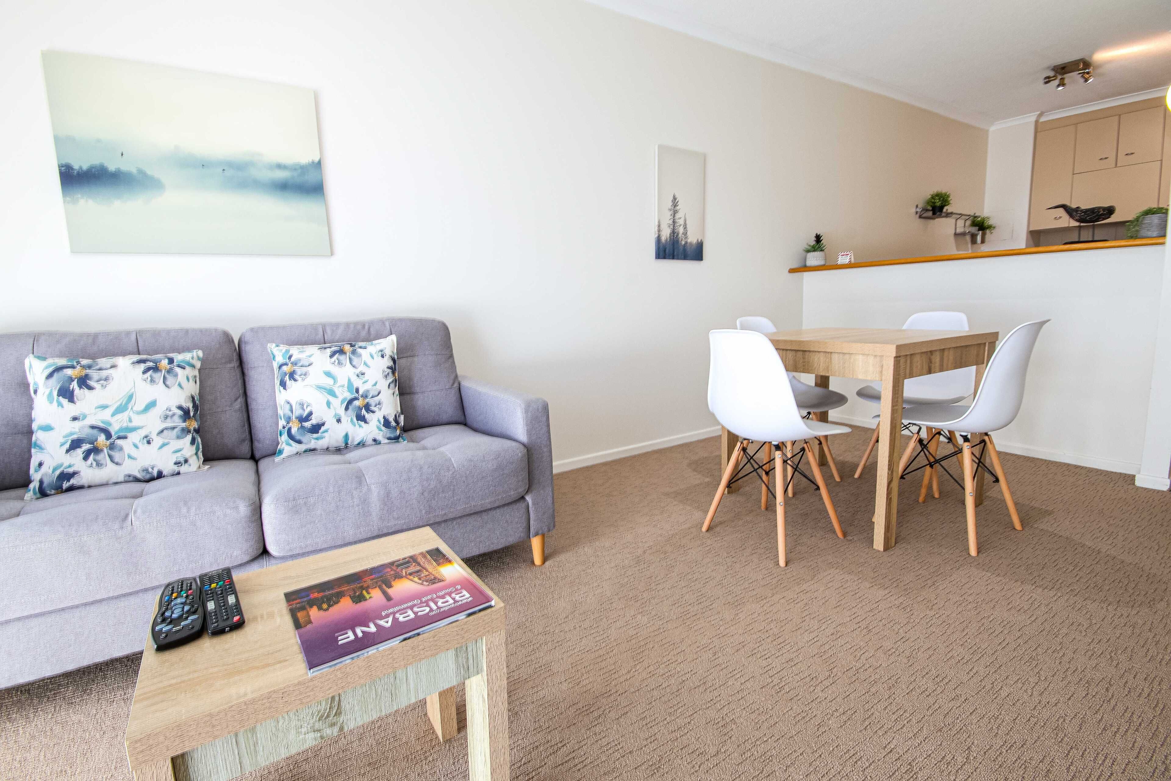 A living room with a grey sofa, a wooden coffee table, and a dining table with white chairs.