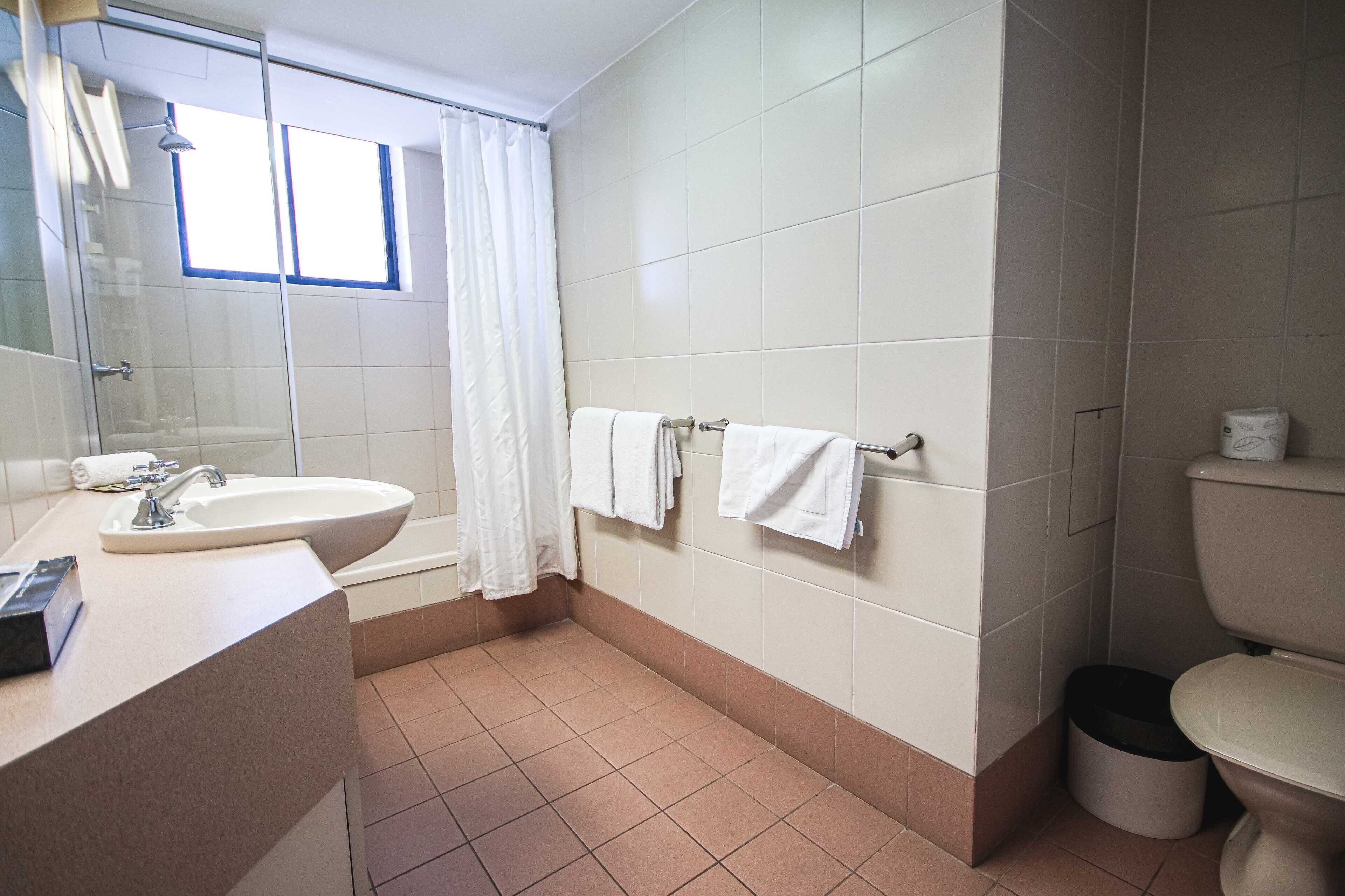 A bathroom with a sink, mirror, and toilet. There is a window with a curtain, and towels are hung on a rack.
