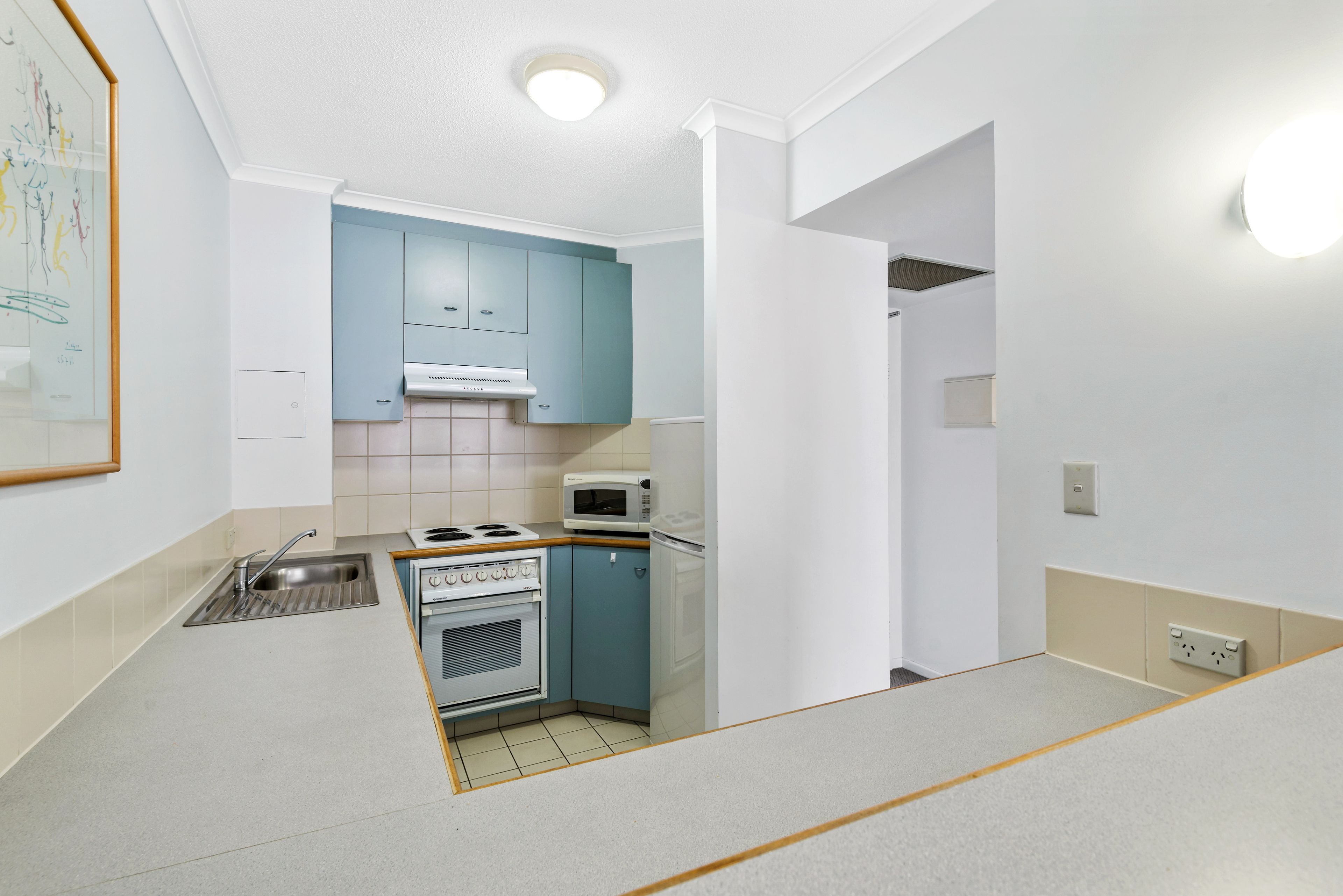 A compact kitchen with white walls, a blue cabinet, a stove, a microwave, and a sink.