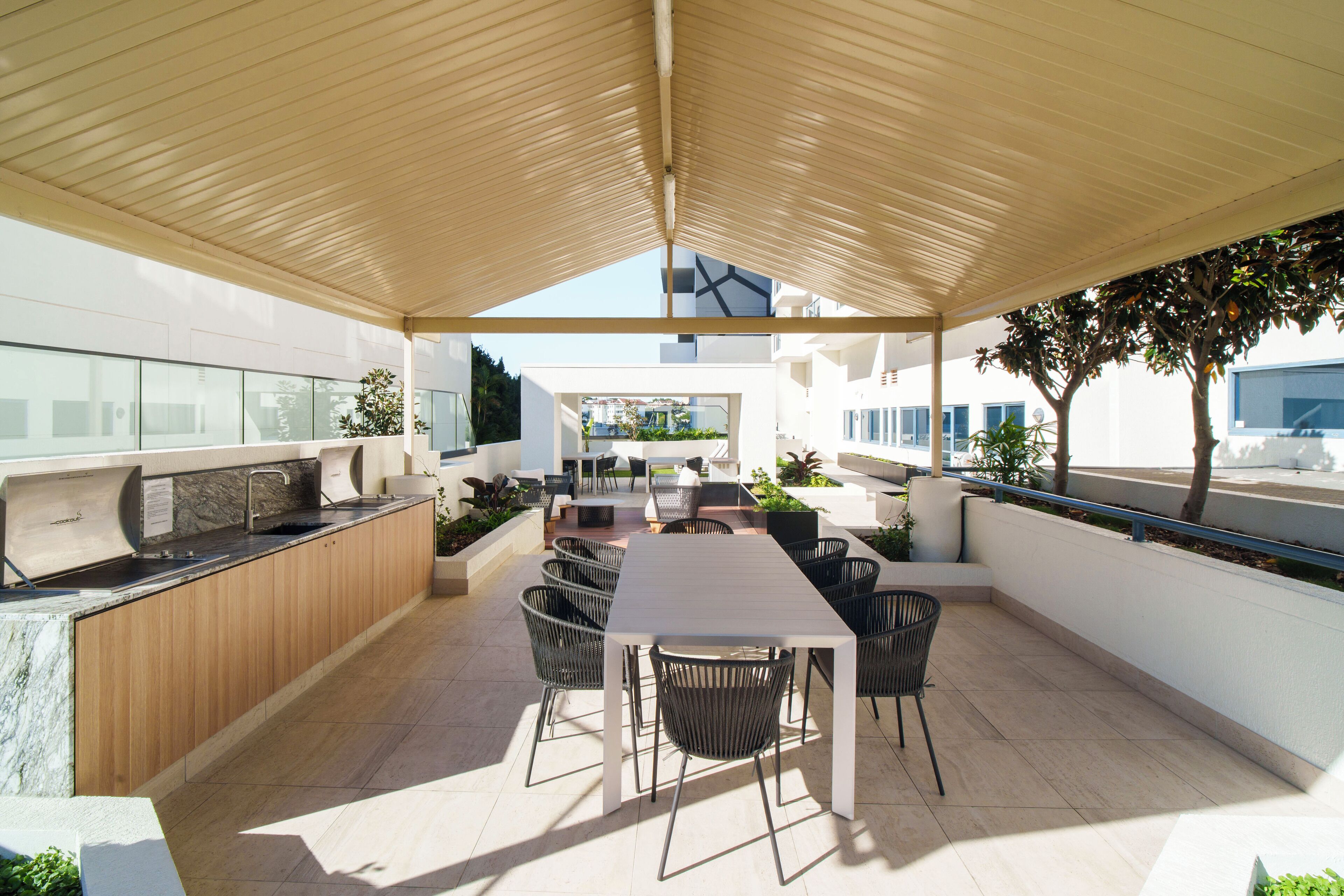 Une terrasse extérieure avec une longue table et des chaises, un comptoir de cuisine intégré et un espace abrité doté d’un plafond en pente.