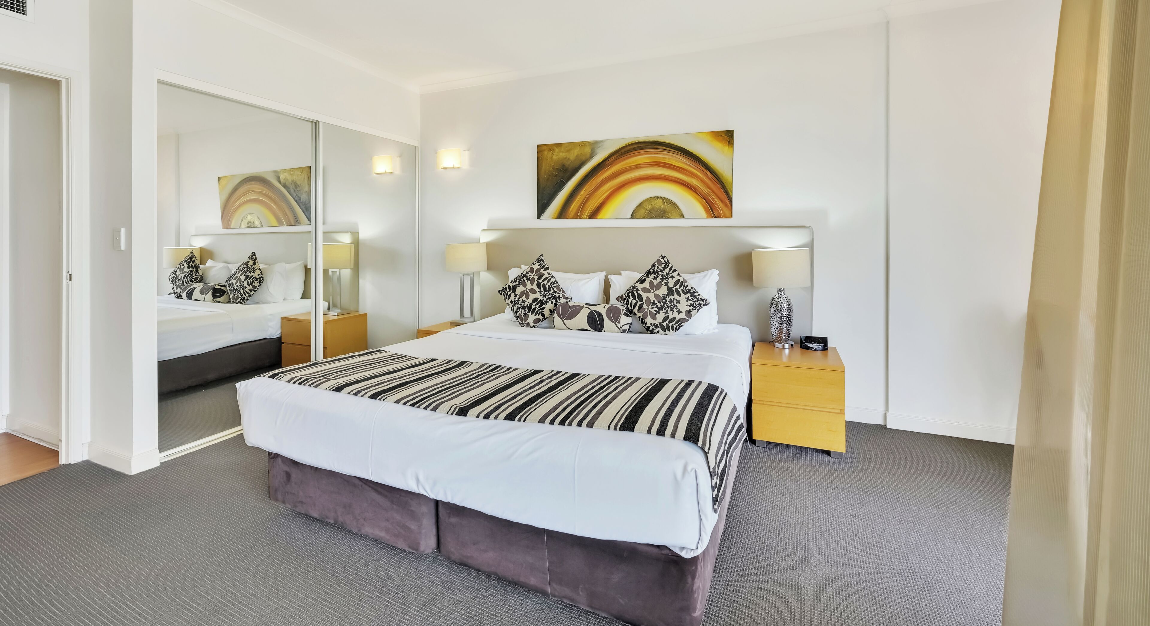 Una camera d'hotel moderna con un letto grande, un comodino, uno specchio e un'opera d'arte appesa al muro.