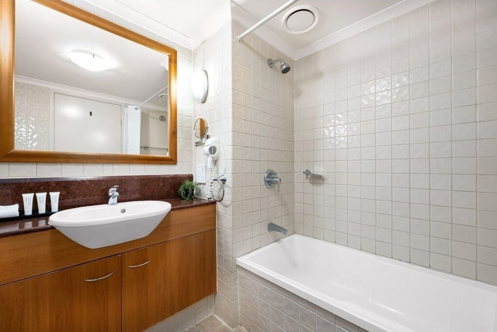 A modern bathroom with a white sink, wooden vanity, and a walk-in shower.