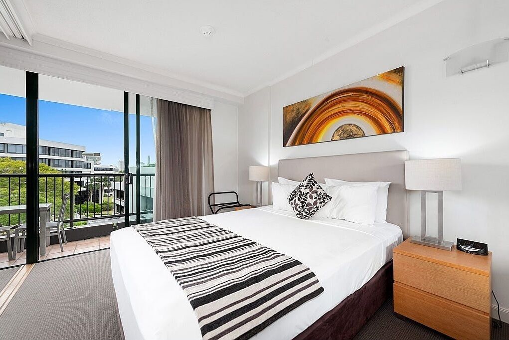 A hotel room with a large bed, a view of the city, and a balcony with outdoor furniture.
