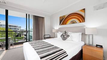 A hotel room with a large bed, a view of the city, and a balcony with outdoor furniture.