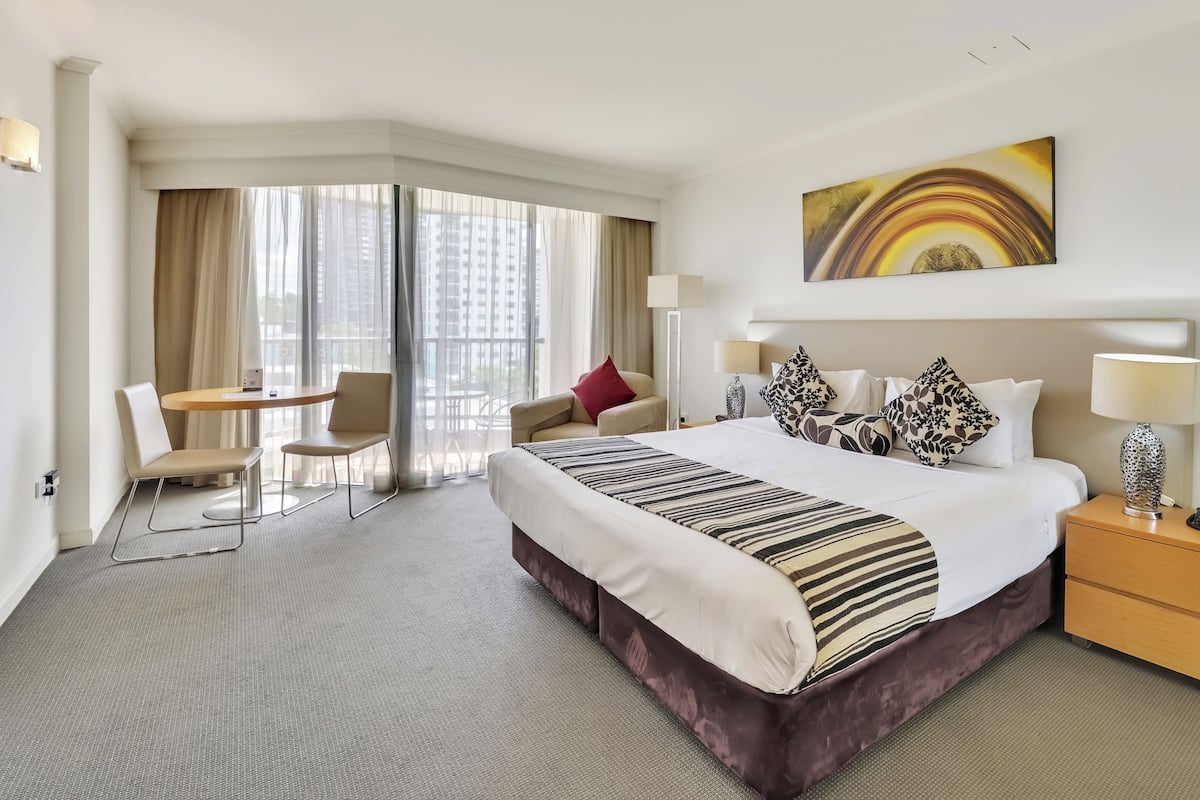 A hotel room with a large bed, a desk, a chair, a nightstand, and a painting on the wall.
