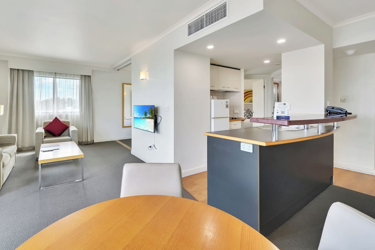 A modern hotel room with a living area, a dining table, a kitchen, and a reception desk.