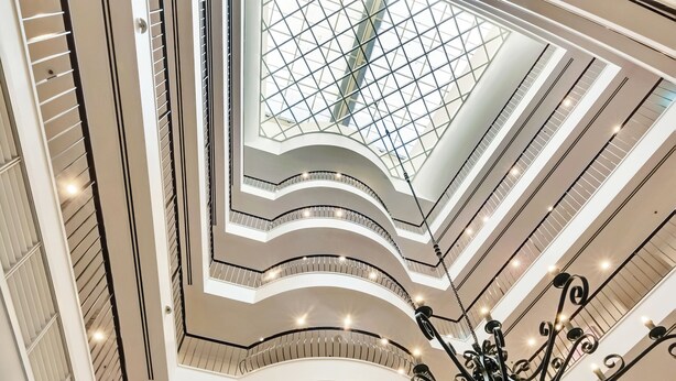 A multi-level atrium with a central glass ceiling, curved balconies, and a chandelier.