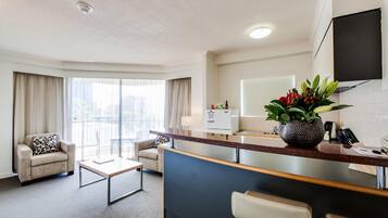 A hotel room with a living area, a kitchenette, a dining area, and a large window with curtains.