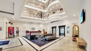 A spacious lobby with a high ceiling, multiple balconies, a reception desk, seating area, and a large chandelier.