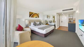 A hotel room with a bed, bedside tables, a TV, a desk, and a kitchenette.