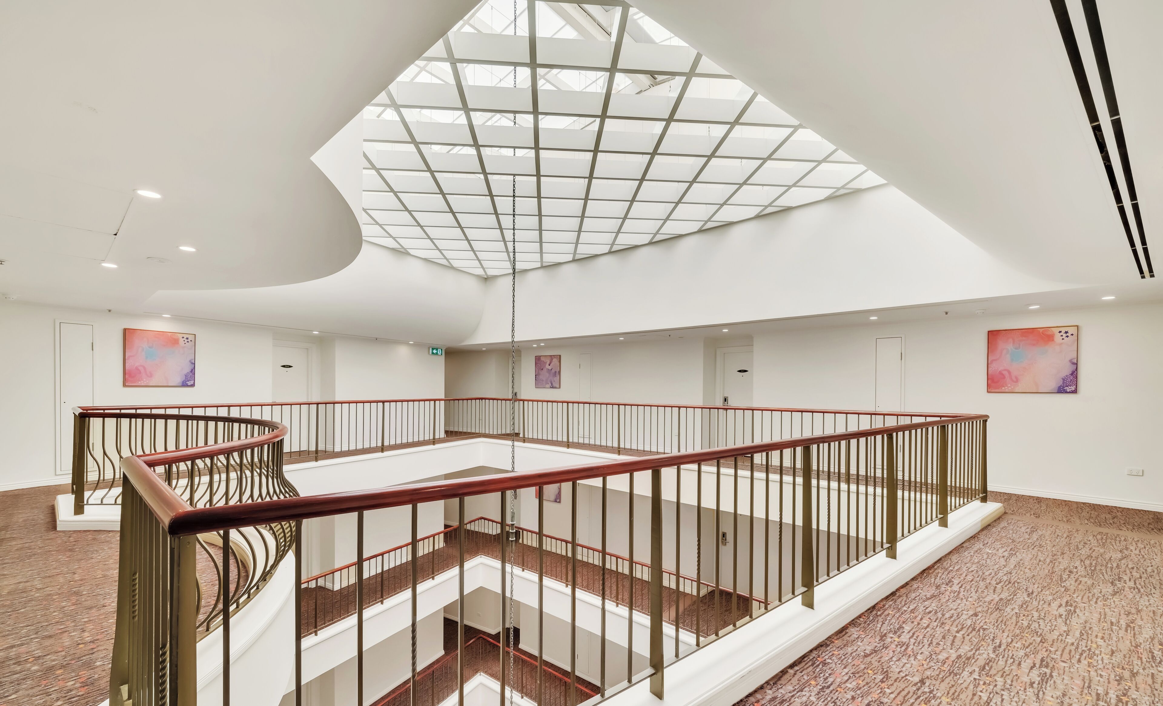 A spacious atrium with a high ceiling, a central open area, and a staircase with a red railing.
