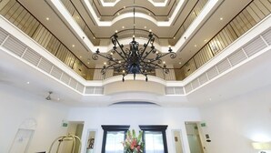 A spacious lobby with a grand chandelier, multiple levels, and a central floral arrangement.