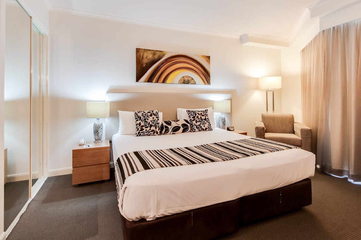A hotel room with a large bed, bedside tables, a chair, a painting on the wall, and a lamp.