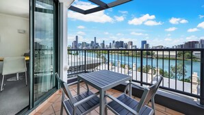 A balcony with a table and chairs, a glass door, and a city view with a river.