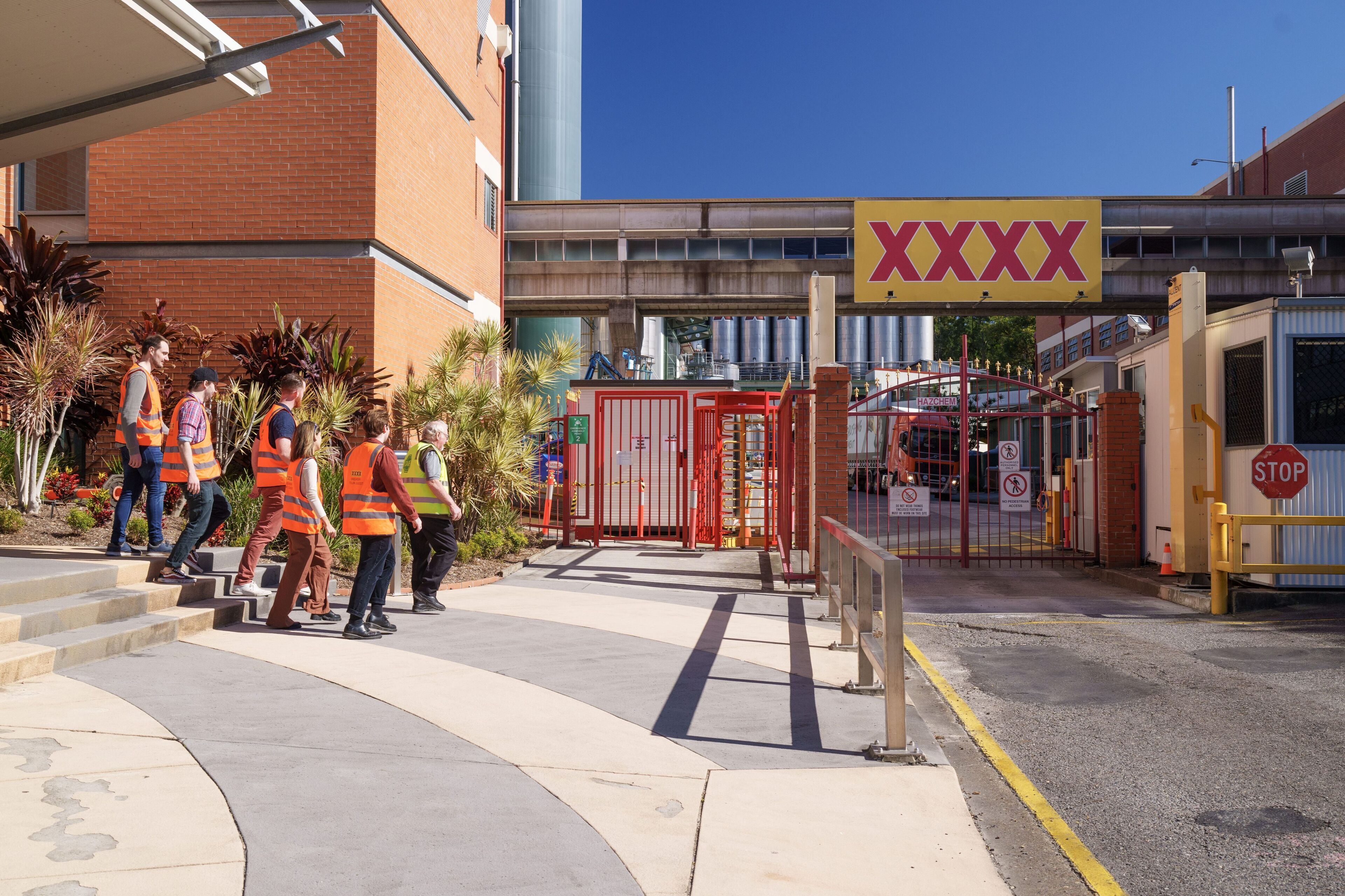 A gated industrial area with a red gate, a stop sign, and a large yellow sign with 'XXXX' on it.