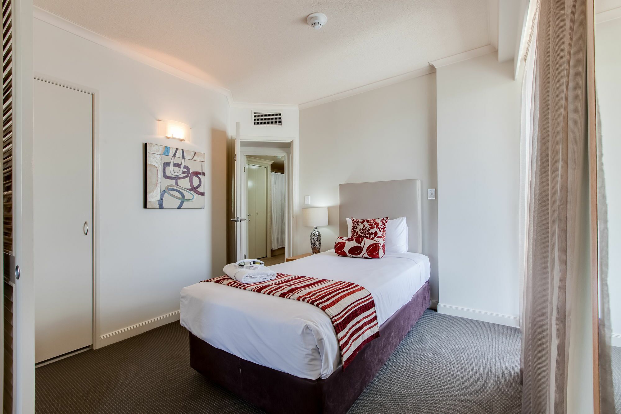 Une chambre d’hôtel avec un lit, une table de chevet, une lampe, un tableau et une porte.