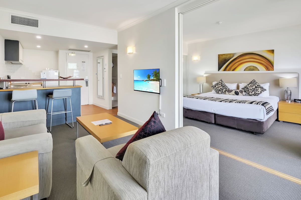 A hotel room with a bed, a desk, a sofa, a TV, and a painting.