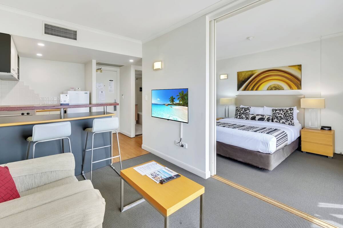 A hotel room with a bed, a desk with a chair, a TV, and a small table with a magazine.