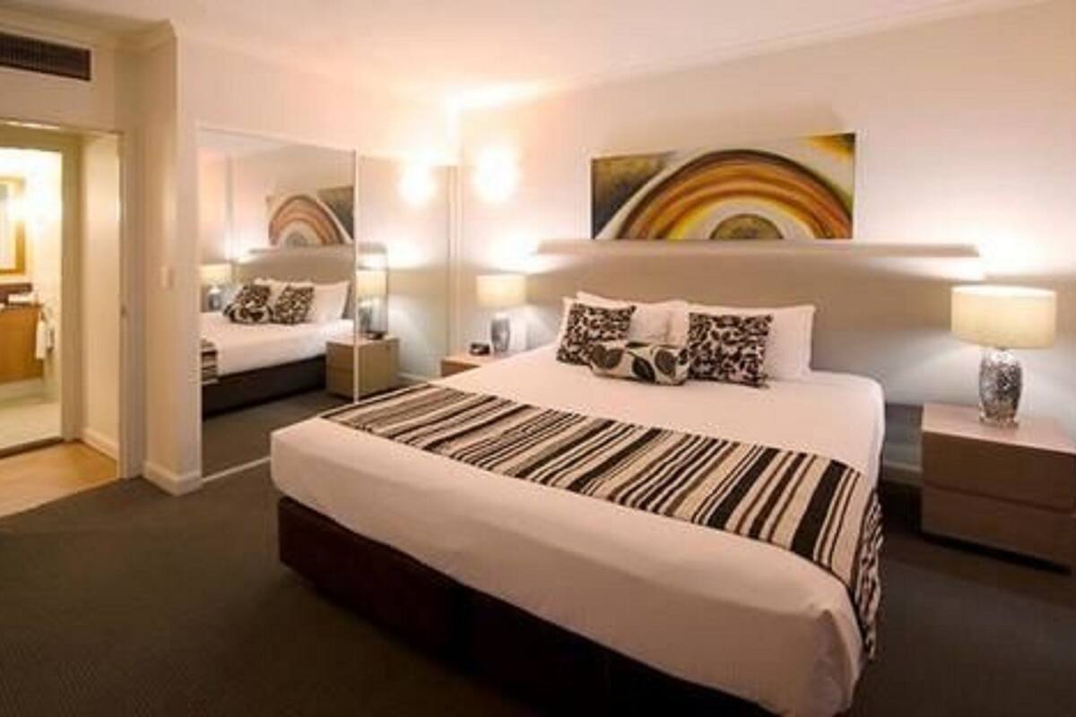 Habitación de hotel con una cama grande, una mesita de noche con lámpara, un espejo y un cuadro en la pared.