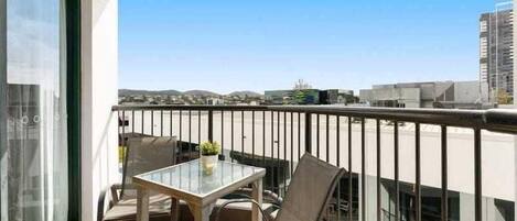 A balcony with a glass table and chairs, a view of the cityscape, and a clear sky.