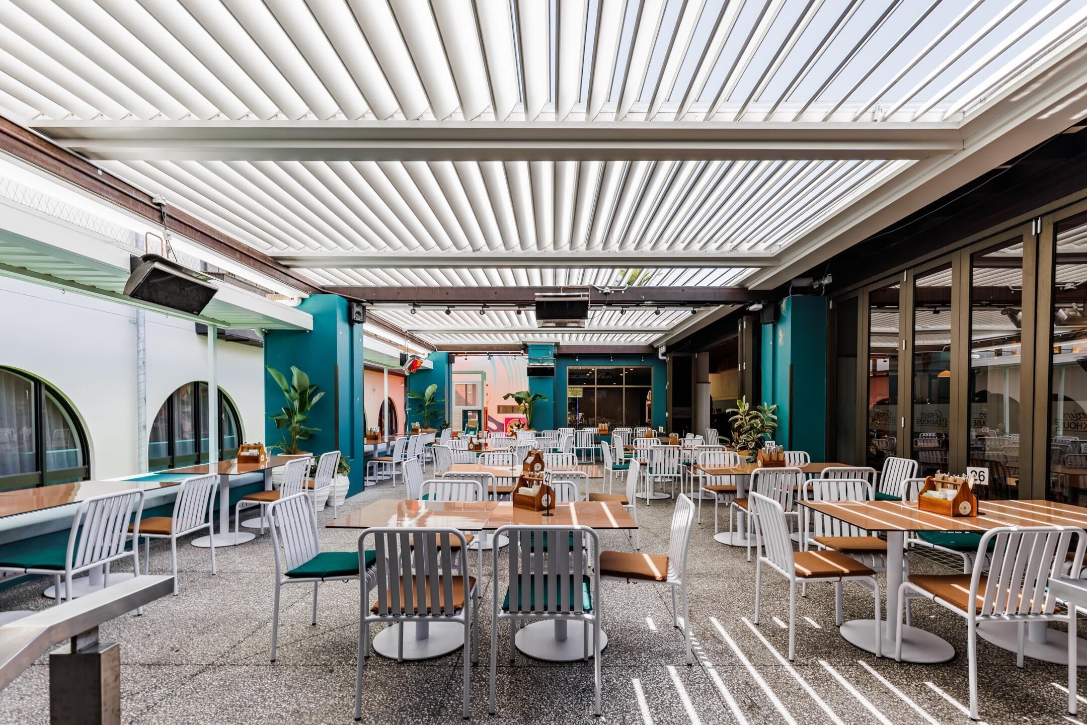 Un vaste espace extérieur aménagé pour les repas, avec plusieurs tables et chaises, un coin salon abrité et de grandes fenêtres.