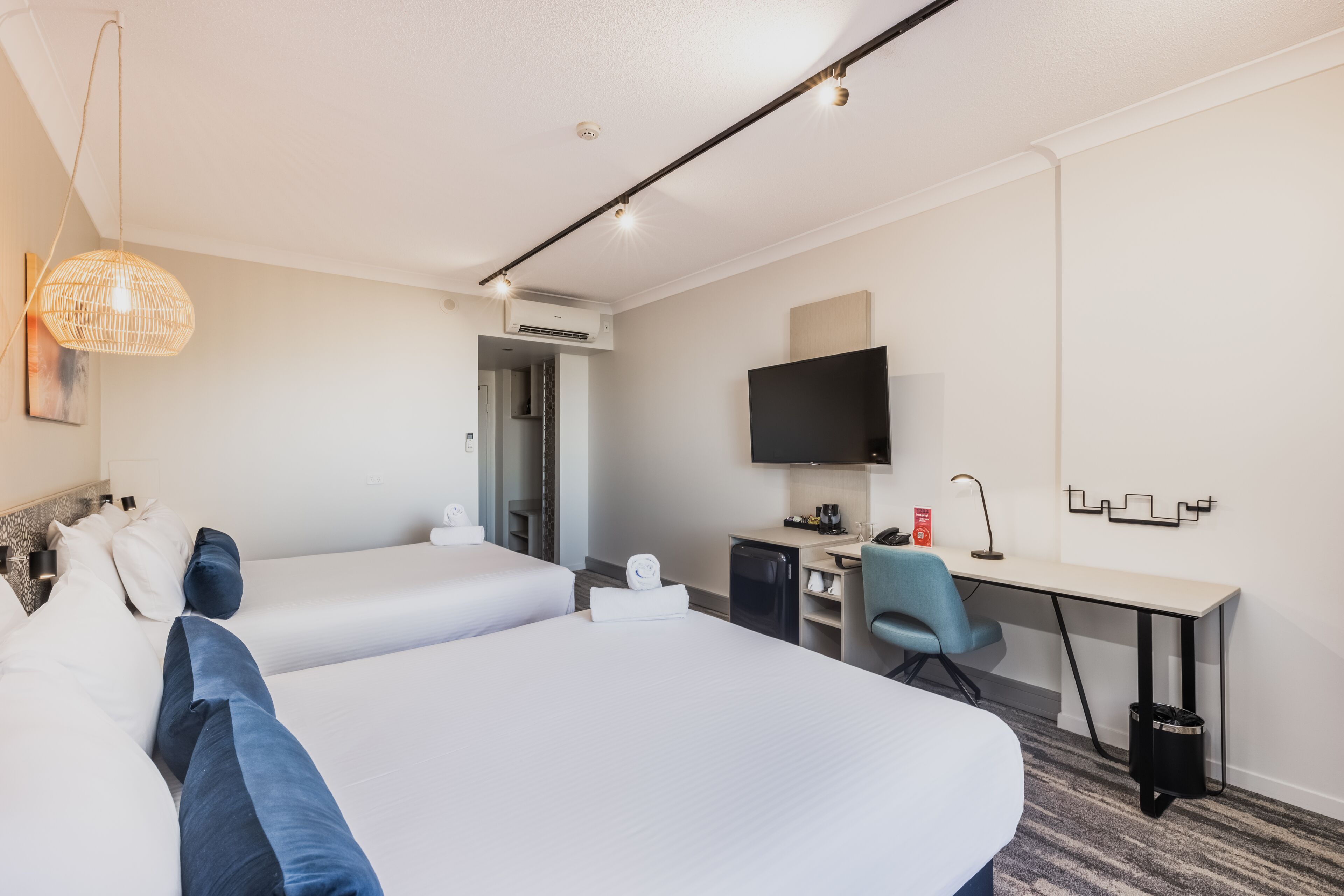 Une chambre d’hôtel avec deux lits, un bureau, une chaise, un téléviseur et un appareil de climatisation.