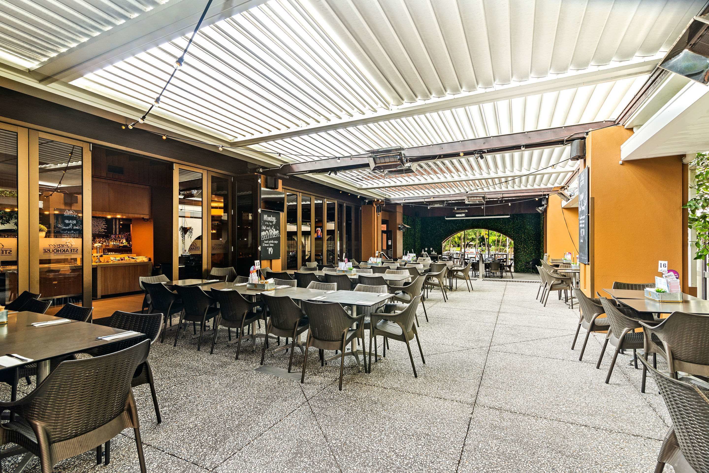 Un café en plein air avec des tables et des chaises, un espace couvert avec un toit, et une vue sur la rue.