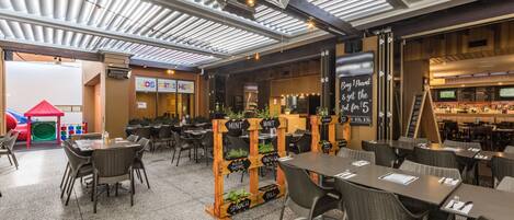 Un restaurante interior con mesas y sillas, una zona de juegos para niños y una barra.