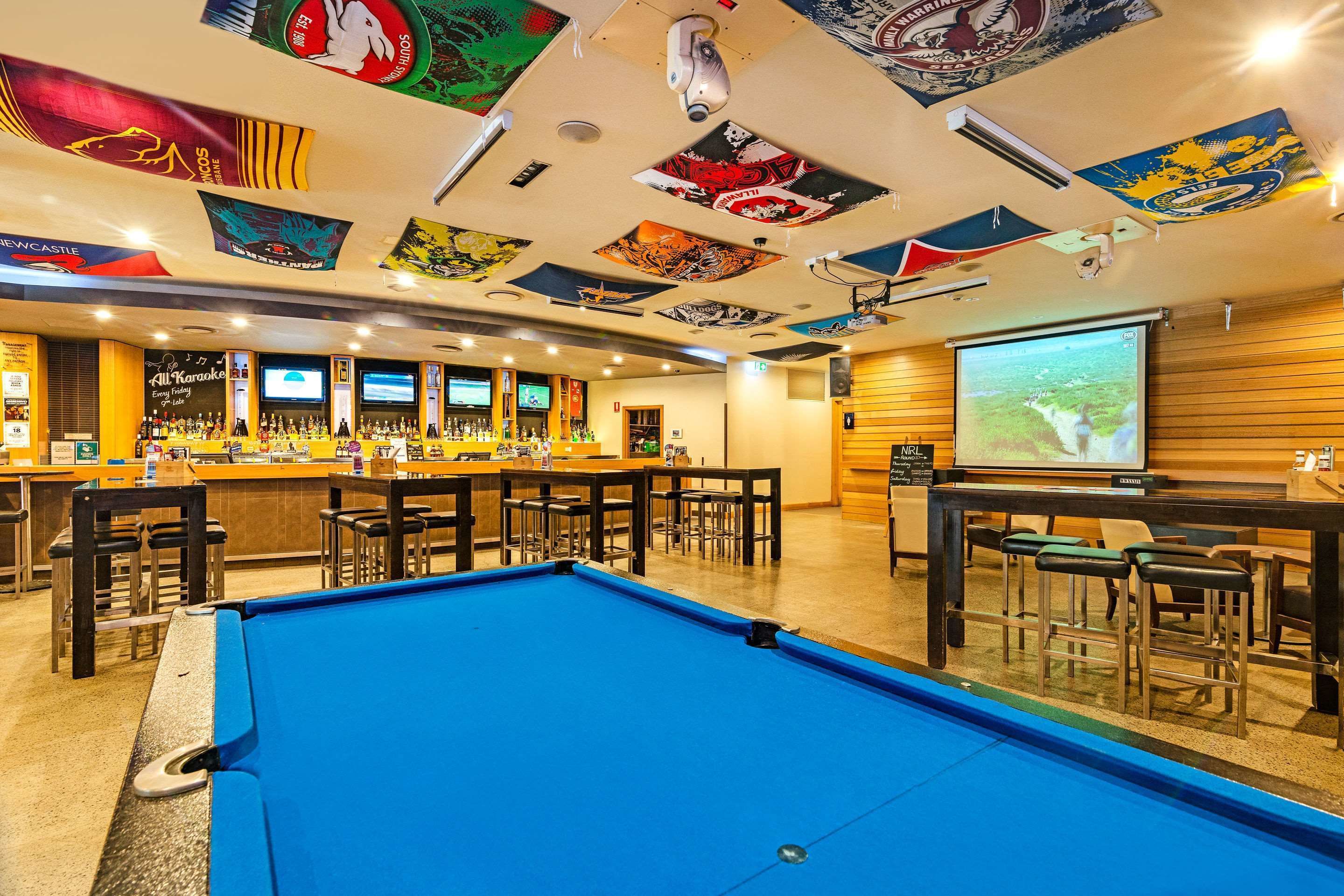 A bar area with a pool table, multiple bar counters, and a projection screen.