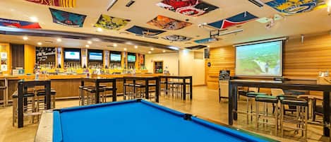 A bar area with a pool table, multiple bar counters, and a projection screen.
