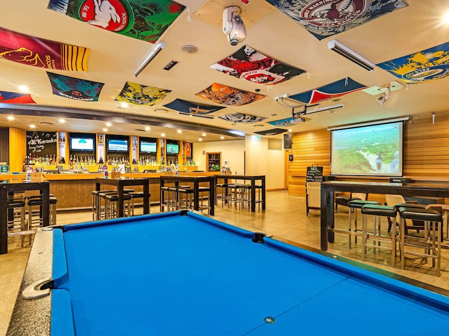 Una zona de bar con mesa de billar, varias barras y una pantalla de proyección.
