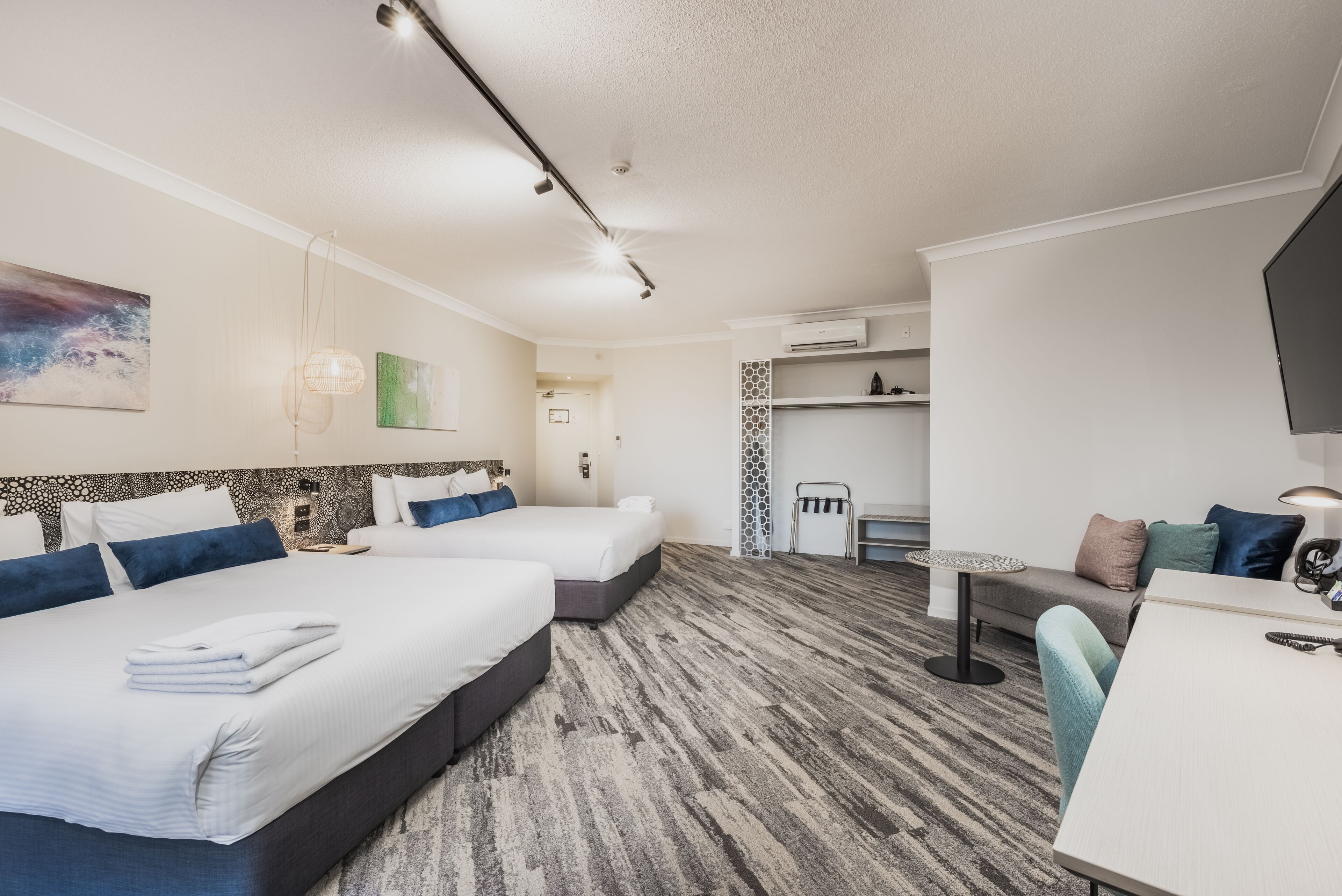 A hotel room with two beds, a desk, a chair, and a small table.