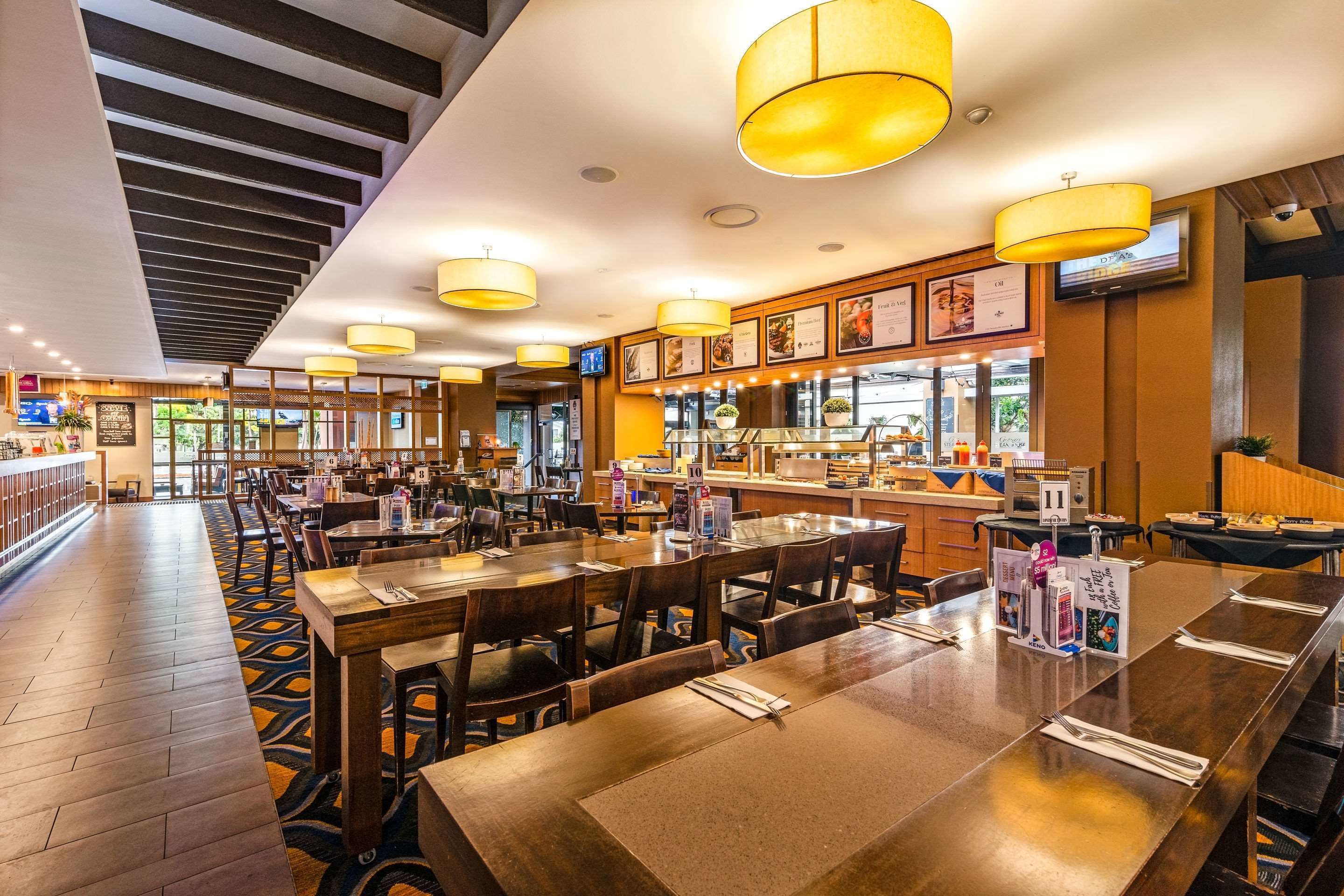 A restaurant with wooden tables and chairs, a bar area, and a staircase leading to an upper level.