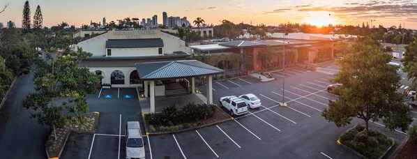 Un hotel con estacionamiento, un acceso cubierto y vistas del horizonte de la ciudad al atardecer.