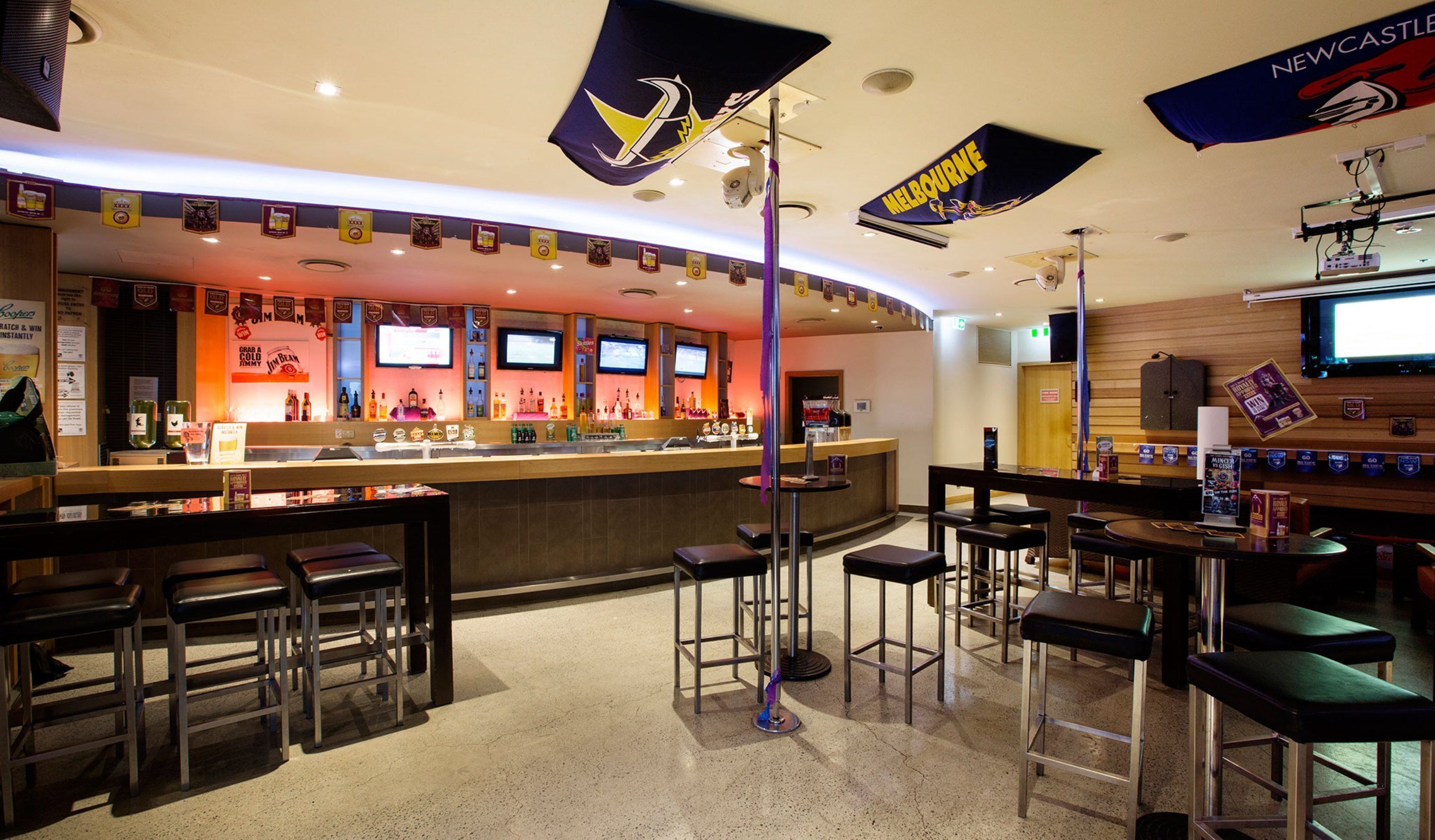 A bar area with multiple seating options, a counter with a variety of bottles, and flags hanging from the ceiling.