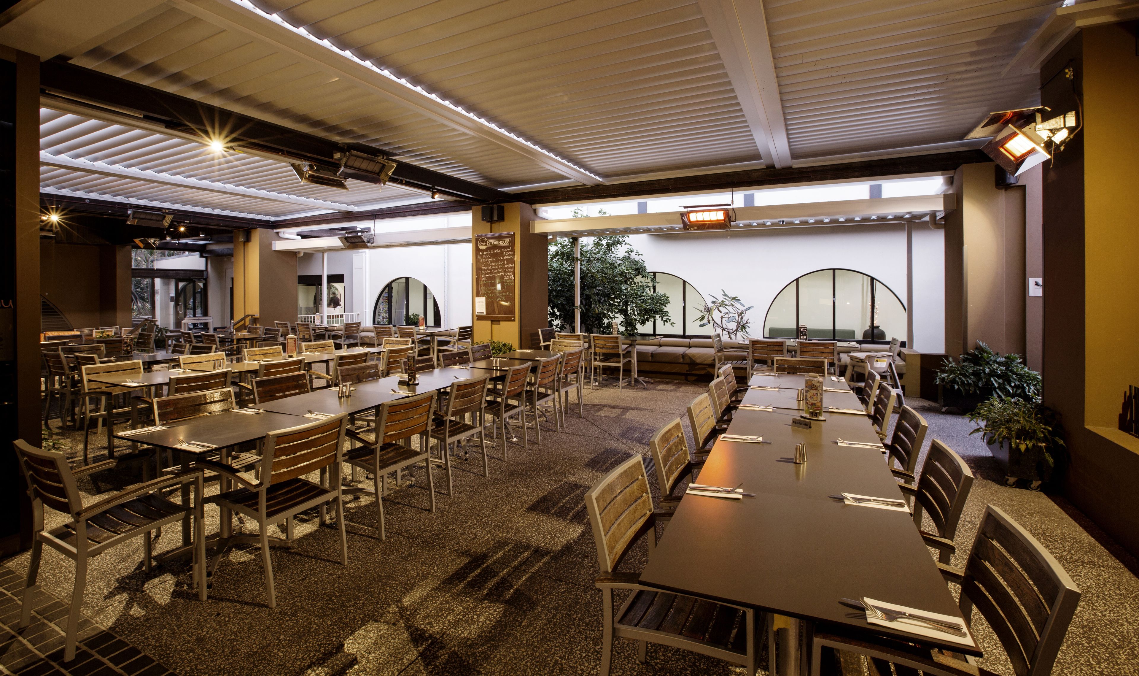 A spacious restaurant with multiple dining tables and chairs, large windows, and a high ceiling with skylights.