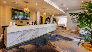 Zona de recepción de un hotel con mostrador de mármol, paneles de madera y una pantalla grande mostrando el menú del restaurante.