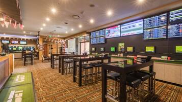 Interior de un casino con múltiples mesas de apuestas, una zona de bar y un mostrador de recepción.