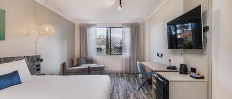 A hotel room with a large bed, a desk, a television, and a window with curtains.