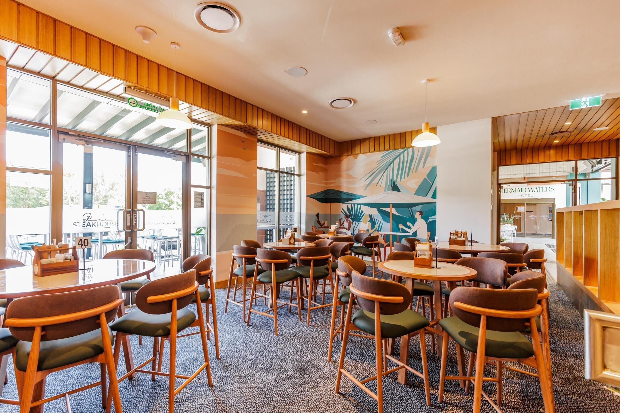 Un restaurant avec des tables et des chaises rondes, de grandes fenêtres et une fresque murale.