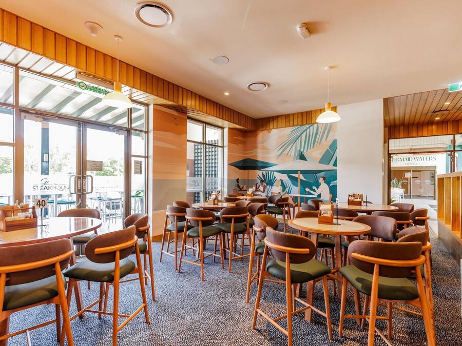 Un restaurant avec des tables et des chaises rondes, de grandes fenêtres et une fresque murale.