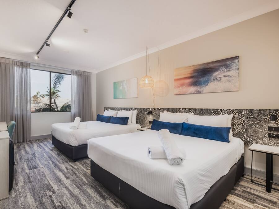 Habitación de hotel con dos camas, un escritorio y un ventanal con cortinas.