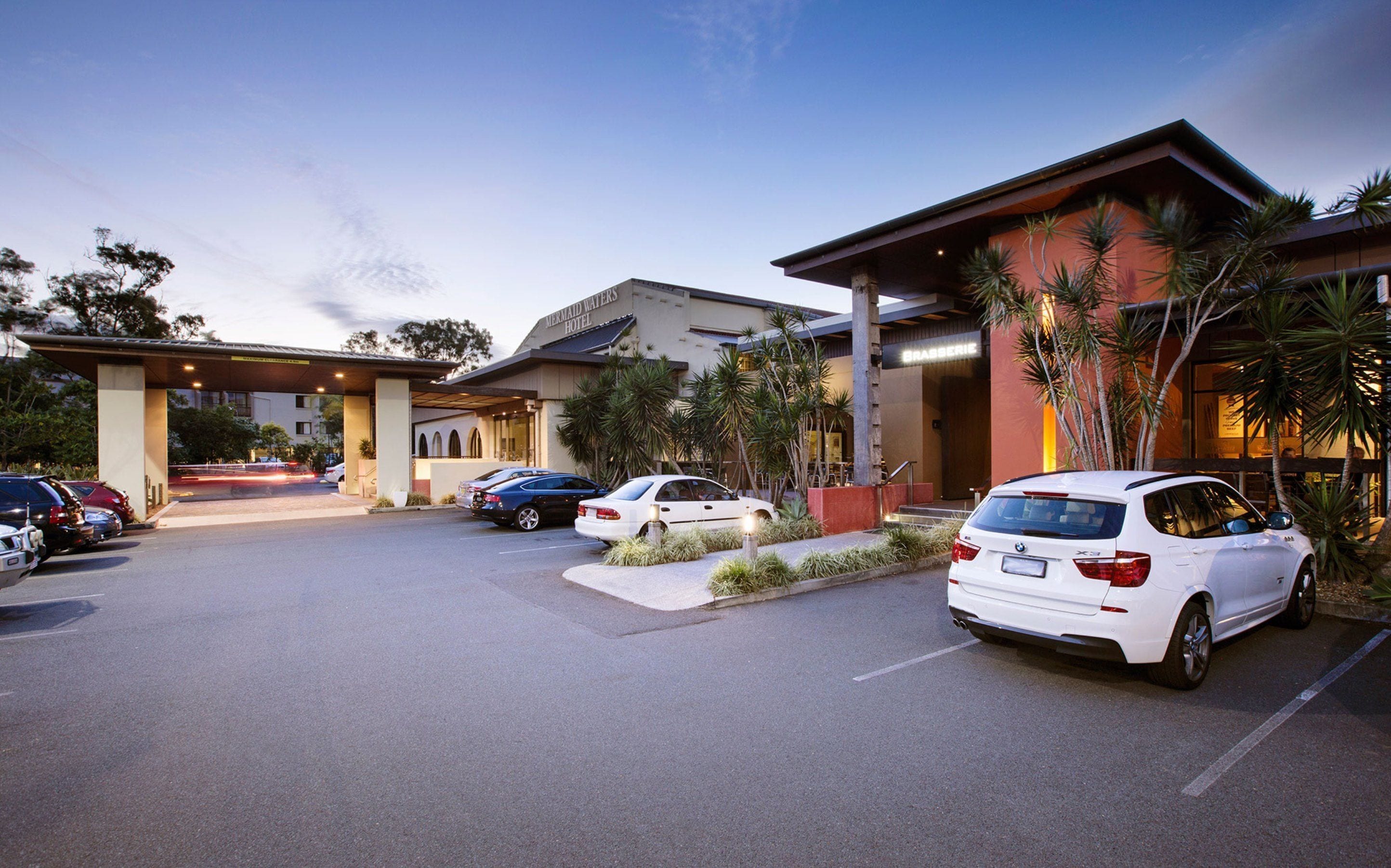 A hotel entrance with a covered parking area, multiple cars parked, and palm trees.