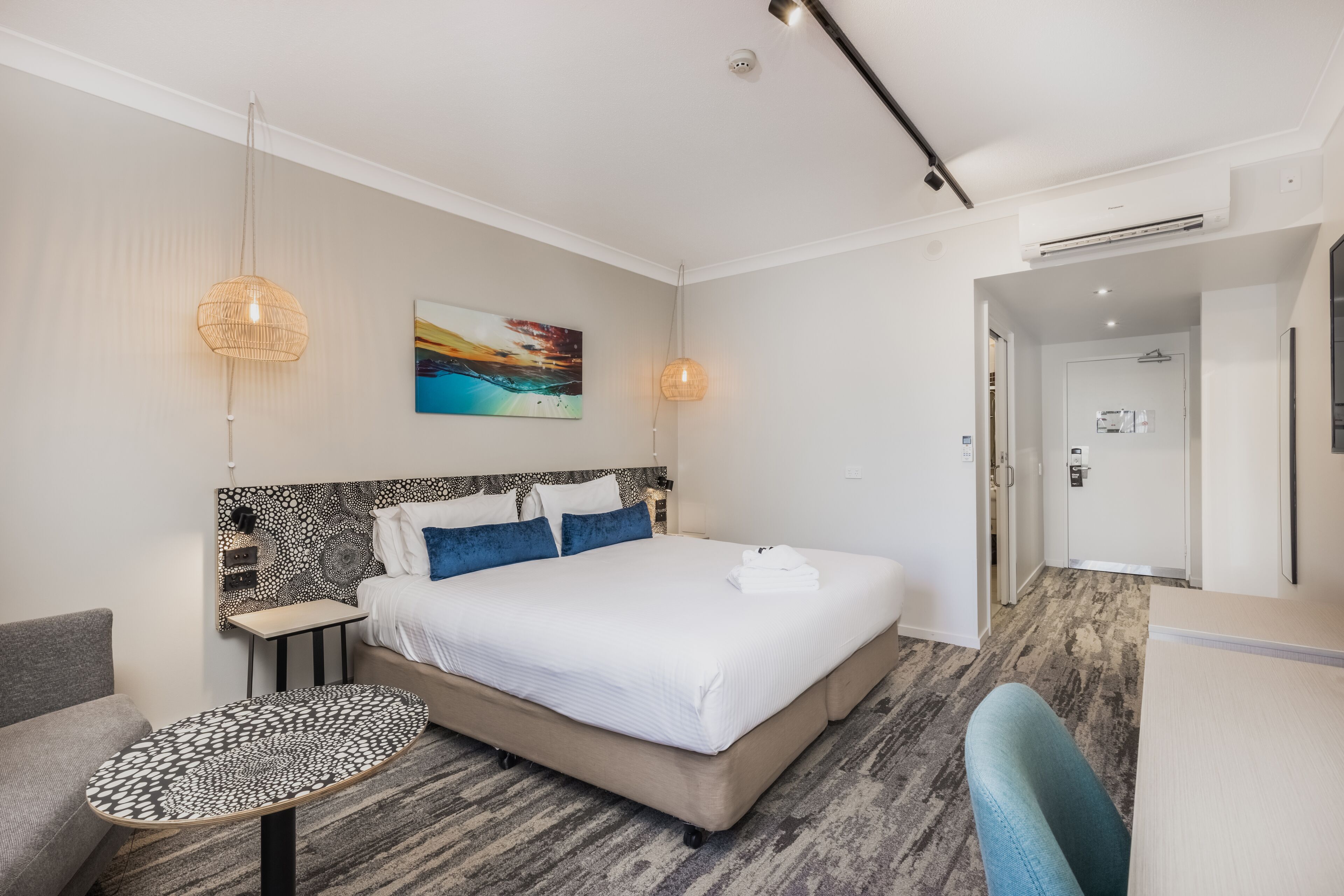 A modern hotel room with a large bed, a small round table, a sofa, and a painting on the wall.