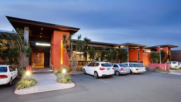 A modern hotel with a parking lot, palm trees, and a building with a prominent orange facade.