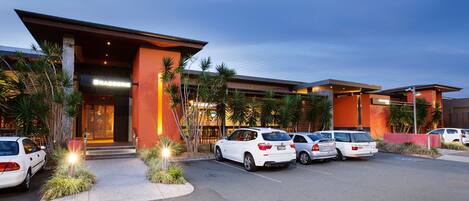 Ein modernes Hotel mit Parkplatz, Palmen und einem Gebäude mit einer auffälligen orangefarbenen Fassade.