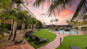 Un área junto a la piscina con sillones de descanso, una piscina y un cielo al atardecer.