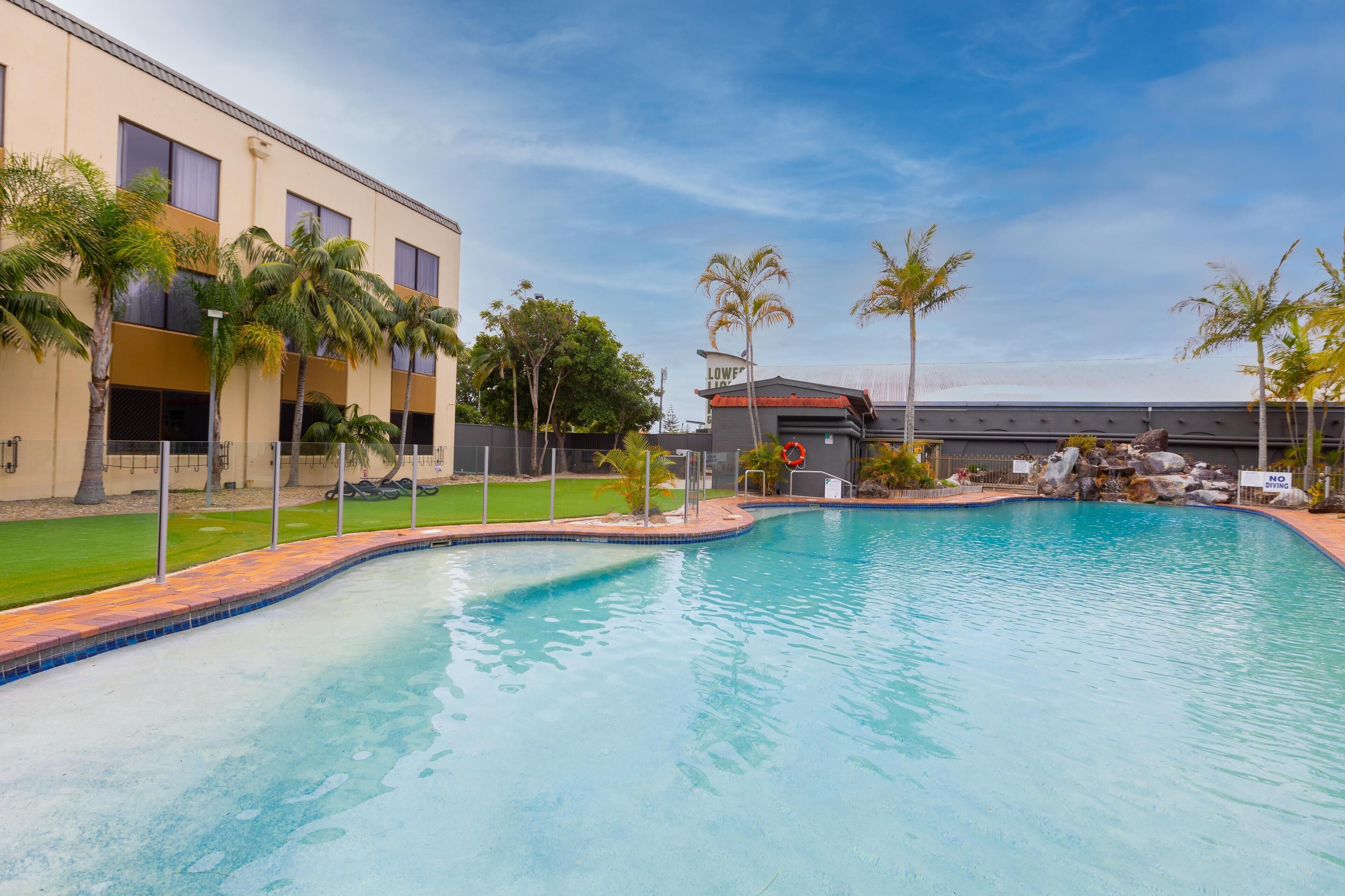 A swimming pool with a curved edge, surrounded by palm trees and a building with a sign that reads "LOWER 10".