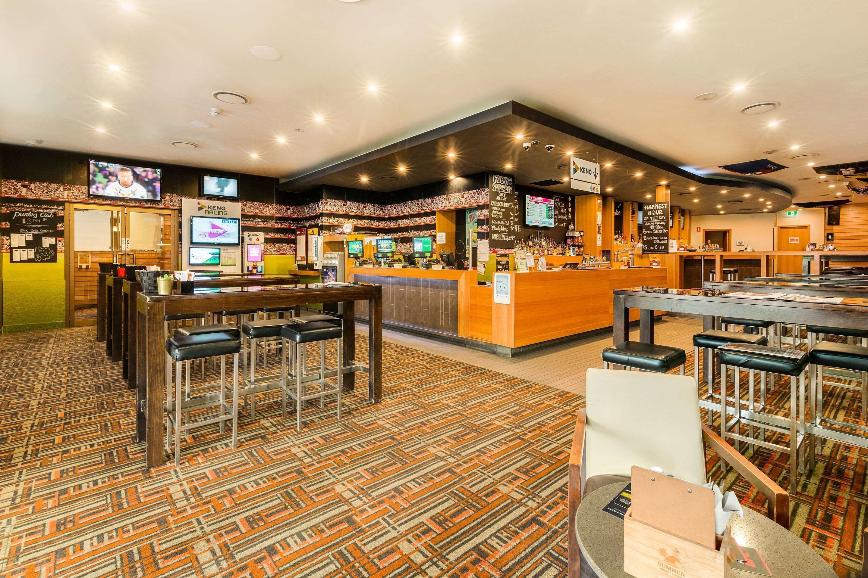 A bar area with multiple seating options, a counter with a menu board, and a television screen displaying a sports event.