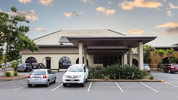 The exterior of the Mermaid Waters Hotel with a covered entrance, parking lot, and a clear sky.